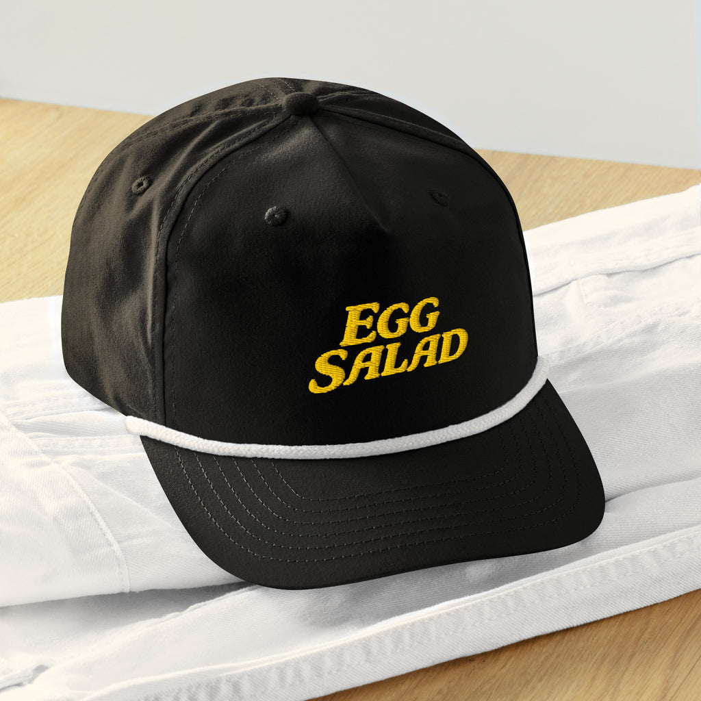 Egg Salad golf rope snapback — black cap with gold big-letter EGG SALAD embroidery, retro tournament style