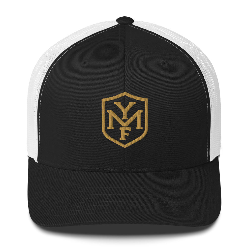 YMF Classic Trucker Hat — black and white mesh trucker with gold embroidered YMF shield monogram, front view